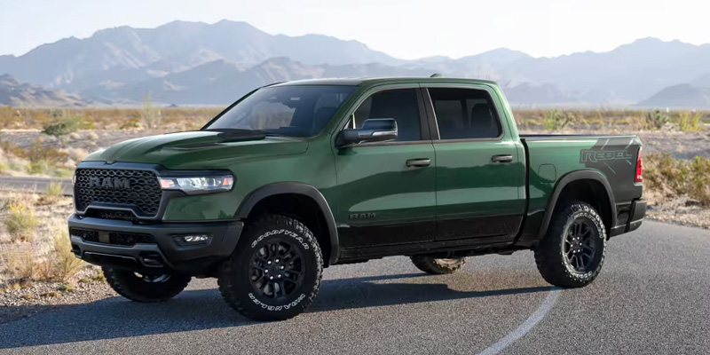 Green Ram 1500 Rebel pickup truck parked on a scenic road with mountains in the background